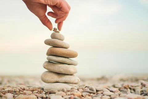 A hand is reaching for a stack of rocks, which are arranged in a pyramid shape Stock Photos