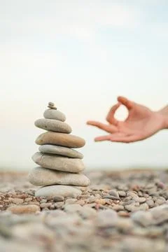 A hand is reaching for a stack of rocks, which are arranged in a pyramid shape Stock Photos