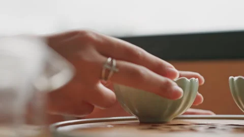 Hand reaching for steaming cup hotel table, ringed fingers lift porcelain teacup Stock Footage 331746492