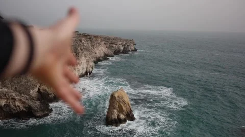Hand reaching toward wild ocean cliffs and crashing waves Stock Footage 327809538