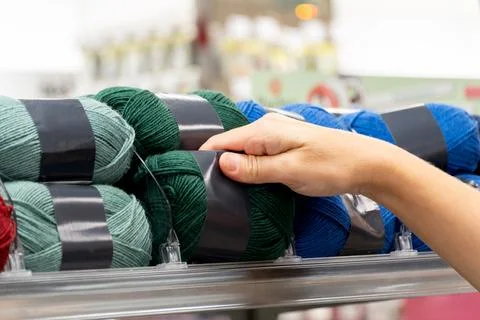 Hand reaching for yarn in a store with multiple colors displayed on a shelf Stock-Fotos