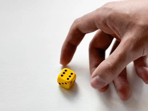Hand reaching for yellow dice on white background - symbol of chance and Stock Photos