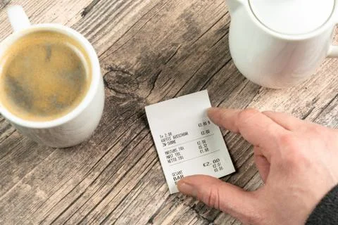 A hand on a receipt on a table with a cup of coffee Stock Photos