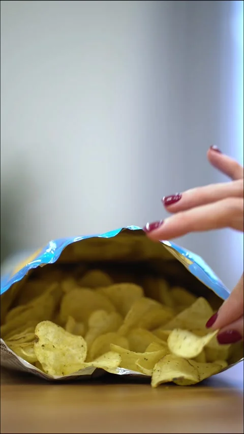 Hand with red nails reaching into open bag of golden potato chips Stock Footage 339982386