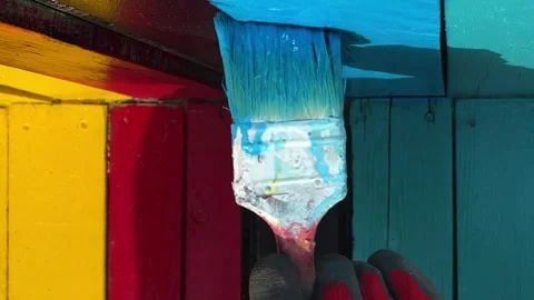 Hand in red work rubber glove applies blue paint to board with brush Stock Footage 346896920