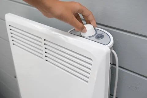 Hand regulating, setting temperature on electric convector, heater thermostate Stock Photos