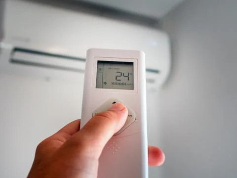 Hand with remote control and adjusting temperature of air conditioner on a wh Stock Photos