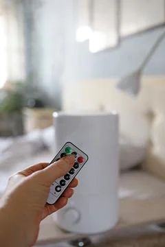 A hand with a remote control in front of an air humidifier on a wall background Stock Photos