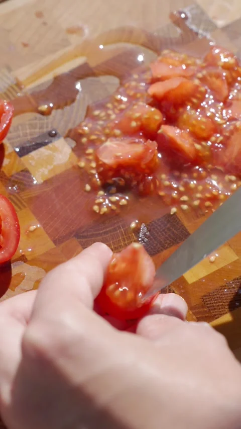 Hand removes pulp from cut tomato with knife on wooden cutting board in sunlight Stock Footage 344408480