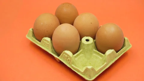 Hand removing an egg from an open egg carton on orange background. Shrinkflation Stock Footage 201853836