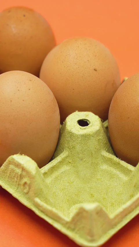 Hand removing an egg from an open egg carton on orange background. Shrinkflation Stock Footage 260054800
