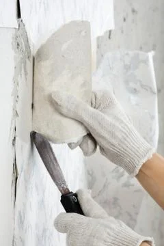 Hand removing old wallpaper from wall with spatula Stock Photos