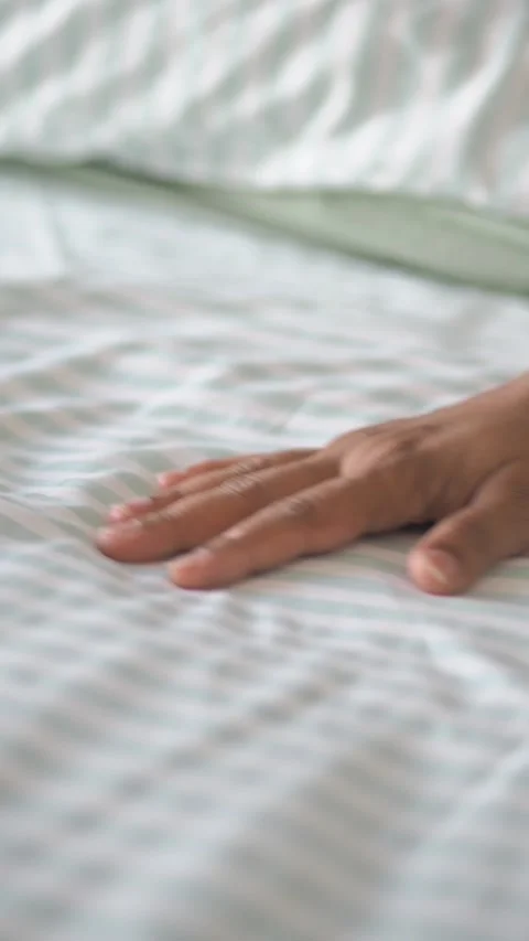 Hand rests on bed surface in simple indoor setting 스톡 동영상 333296517
