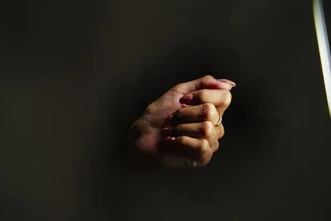 A hand with a ring on it is shown in a dark room. The hand is clenched and .. Stockfoto's