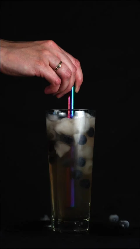 Hand with ring stirring drink with ice and berries on black background 스톡 동영상 220892237