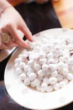 A hand with a ring taking small white sweets from the white plate. Many round Stock Photos