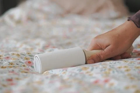 Hand Rolling Lint Roller Over Floral Bedspread Bedding For Quick Home Clean.. Stock Photos