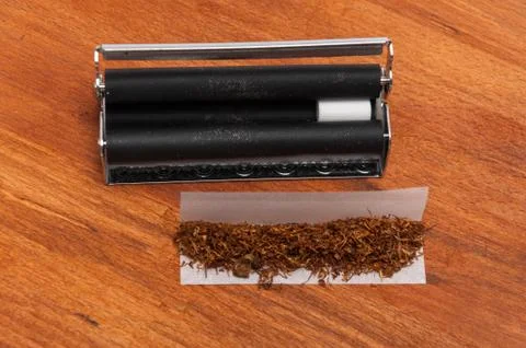 Hand rolling machine with a filter and tobacco on the paper on the wood Stock Photos
