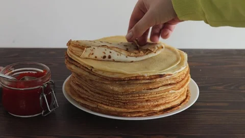 Hand rolling thin crepe with red caviar filling next to tall stack of pancakes Stock Footage 309301813
