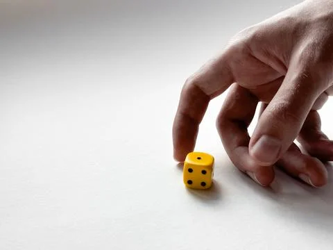 Hand rolling yellow dice on white surface for luck and strategy Stock Photos
