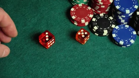 Hand rolls two dice across a green felt table surrounded by colorful poker chips Stock Footage 338015986