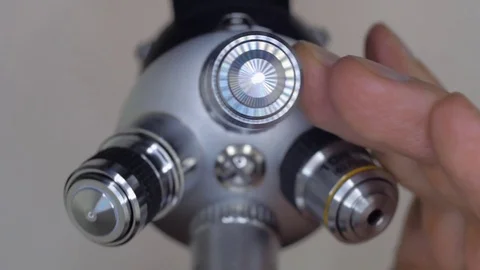 A hand rotates a block of microscope lenses one of them glows brightly Stock Footage 82722609