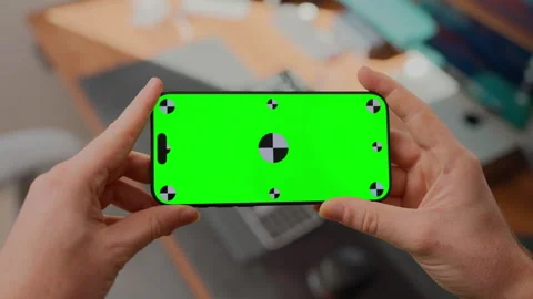 Hand Rotates Smartphone with Green Screen Mockup in Modern Office Workspace Stock Footage 345846933