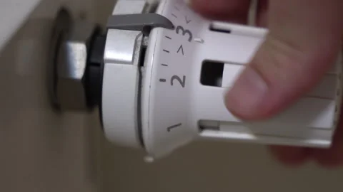 Hand rotating a radiator thermostat to increase heating, illustrating energy use Stock Footage 322134197