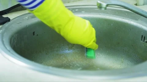 A hand in a rubber glove washes limescale and rust from the surface of the sink 库存影片 130878700