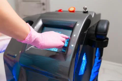 A hand in rubber gloves presses at the sensor screen of the laser device. Clo Stock Photos