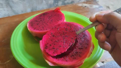 Hand scooping fresh red dragon fruit with a spoon on a green plate Stock Footage 344634767