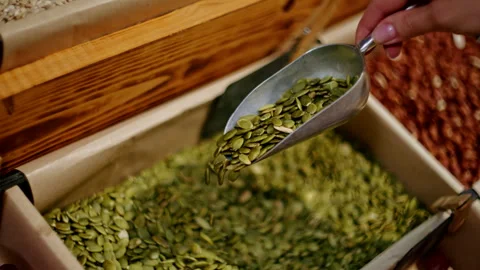 Hand scooping pumpkin seeds from bulk bin in organic grocery store. Close-up of Stock Footage 291587107