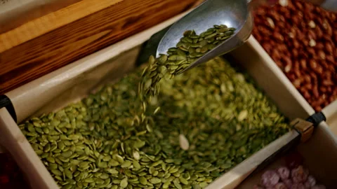 Hand scooping pumpkin seeds from bulk bin in organic grocery store. Close-up of Stock Footage 291587351