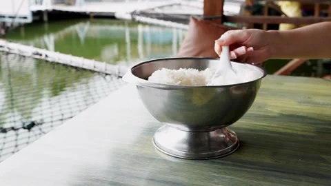 Hand scooping steamed white jasmine rice from a stainless steel bowl on a w.. Video stock 335005736