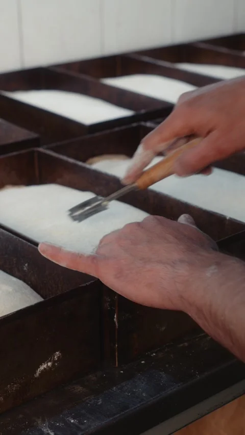 Hand scoring bread dough with a blade in metal baking trays Stock Footage 344313042