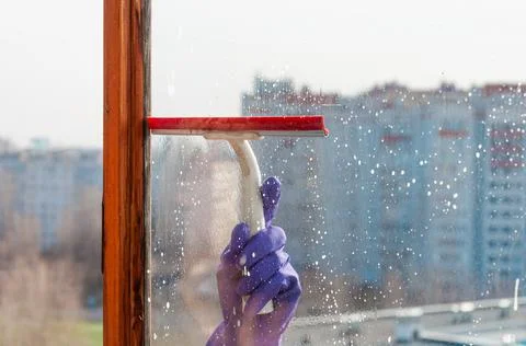 A hand scrapes the soap suds off the window pane Stock Photos