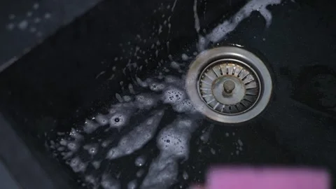 A hand scrubs a kitchen sink with a sponge while bubbles form around the drain. 動画素材 337642838