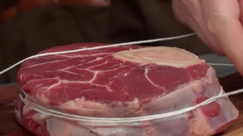 Hand securing an Osso Buco steak with kitchen twine Stock Footage 314111727