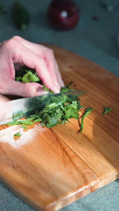 A hand is seen chopping fresh herbs on a wooden cutting board in a kitchen. Stock Footage 338304169