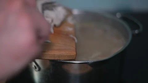 A hand is seen guiding shredded chicken from a wooden board into a pot filled Stock Footage 338301368