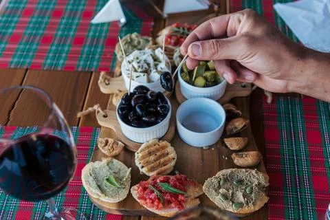 Hand selecting black olive from Mediterranean appetizer board with red wine Stock Photos