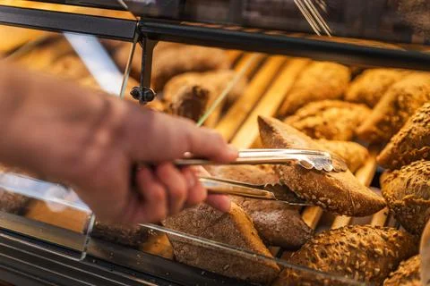Hand Selecting Crusty Bread with Serving Tongs in Bakery Display Stock Photos