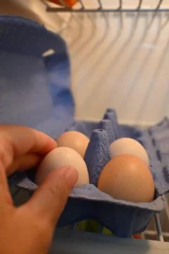 Hand selecting eggs from an open refrigerator Stock Photos