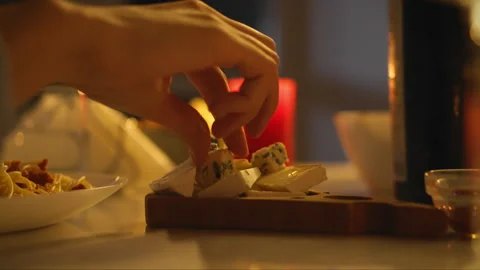 Hand selecting gourmet cheese at an evening gathering with warm candlelight Stock Footage 323806296