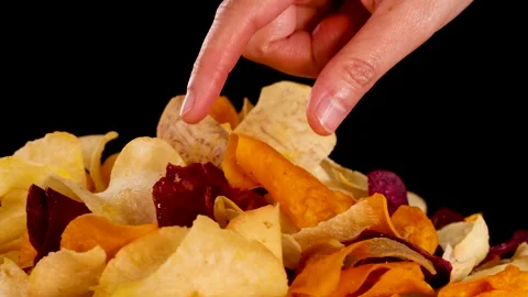 Hand Selecting Mixed Root Vegetable Chips Against Black Background Stock Footage 320594402