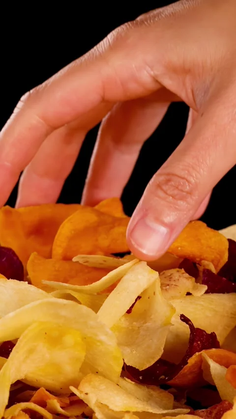 Hand Selecting Mixed Root Vegetable Chips Against Black Background Stock Footage 321322985