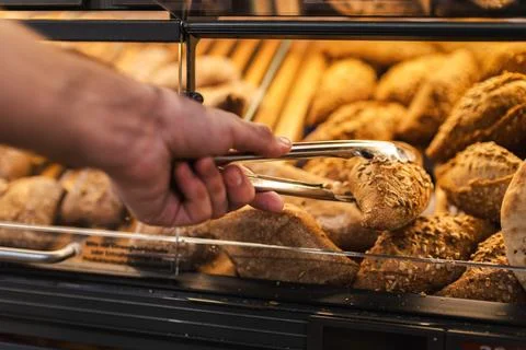 Hand Selecting Rustic Bread with Tongs at Bakery Display Fotos Stock