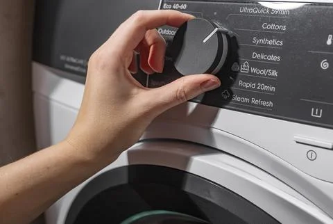 Hand selecting washing program on machine panel. Fingers turning control knob Foto stock