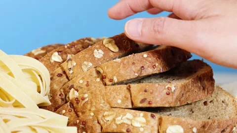 Hand selects slice of hearty whole grain bread from stack next to fettuccin.. Stock Footage 334352627