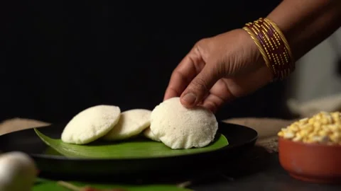 A hand serving fresh steamed idli onto a banana leaf plate Vídeo Stock 340958434